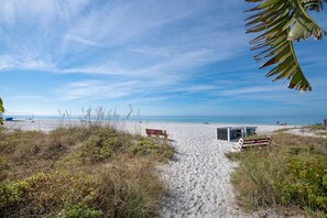 A sandy beach path leading to a small structure with a bench, surrounded by vegetation.