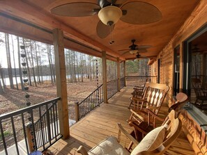 Terraza de madera con mobiliario exterior y vistas a un bosque y un lago.