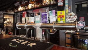 Un bar doté d’un robinet pour servir la bière, entouré de différentes étiquettes de bière et muni d’une étagère remplie de bouteilles.