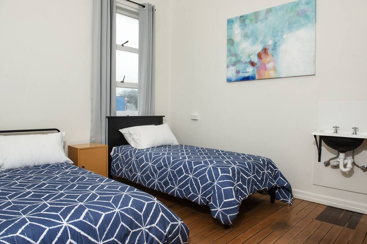 Quarto com duas camas, uma janela, um quadro e uma pia.
