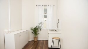 Une petite cuisine blanche, avec un plancher en bois, un comptoir blanc et un tabouret de bar.