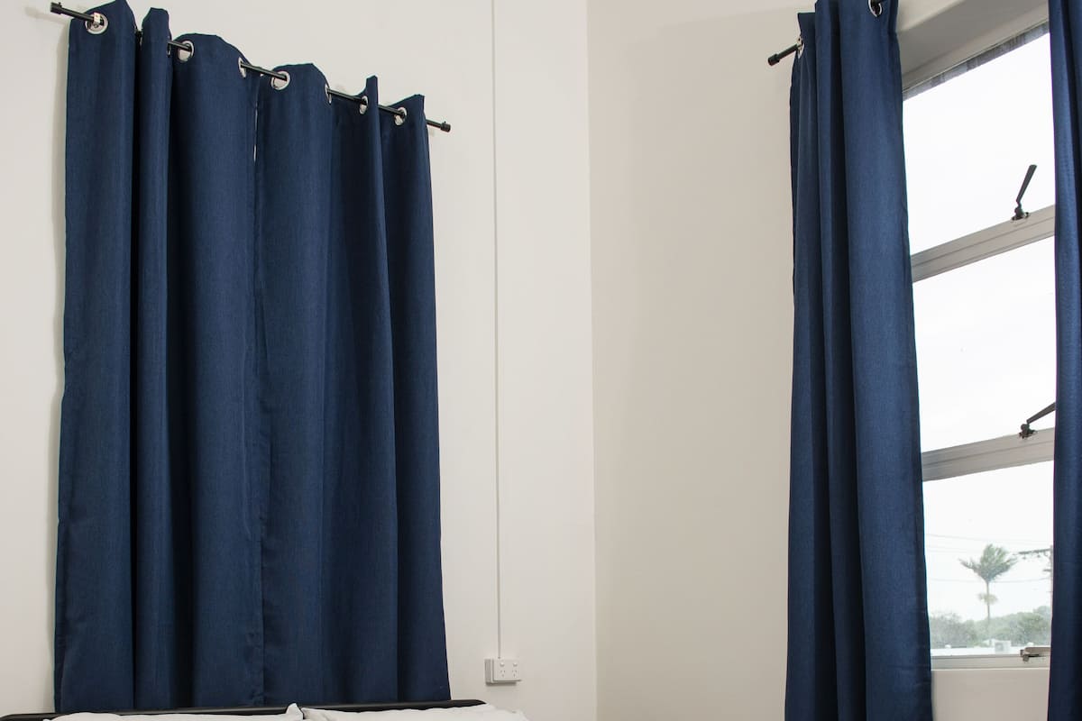 Quarto com cama, roupa de cama branca e cortinas azuis.