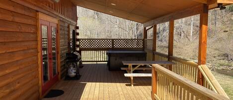 A wooden deck with a picnic table and grill, surrounded by a wooden fence and overlooking a forested area.