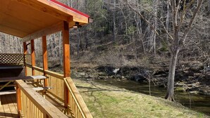 A wooden deck with a picnic table and benches overlooking a river and forested area. - New 2/2 Log Cabin, Rushing Trout Stream, Hot Tub, Fireplace, 8 Acres, WiFi (Deep Gap)