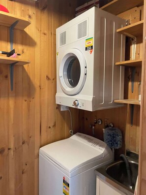 Een kleine wasruimte met een voorlader wasmachine en een droger, beide wit, in een kamer met houten lambrisering.