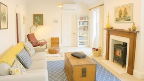 A cozy living room with a sofa, a wooden chest, a fireplace, a bookshelf, and a door leading to another room. - Historic 3-Bed 'Bostane Cottage' 5 minutes to City. (West Hobart)