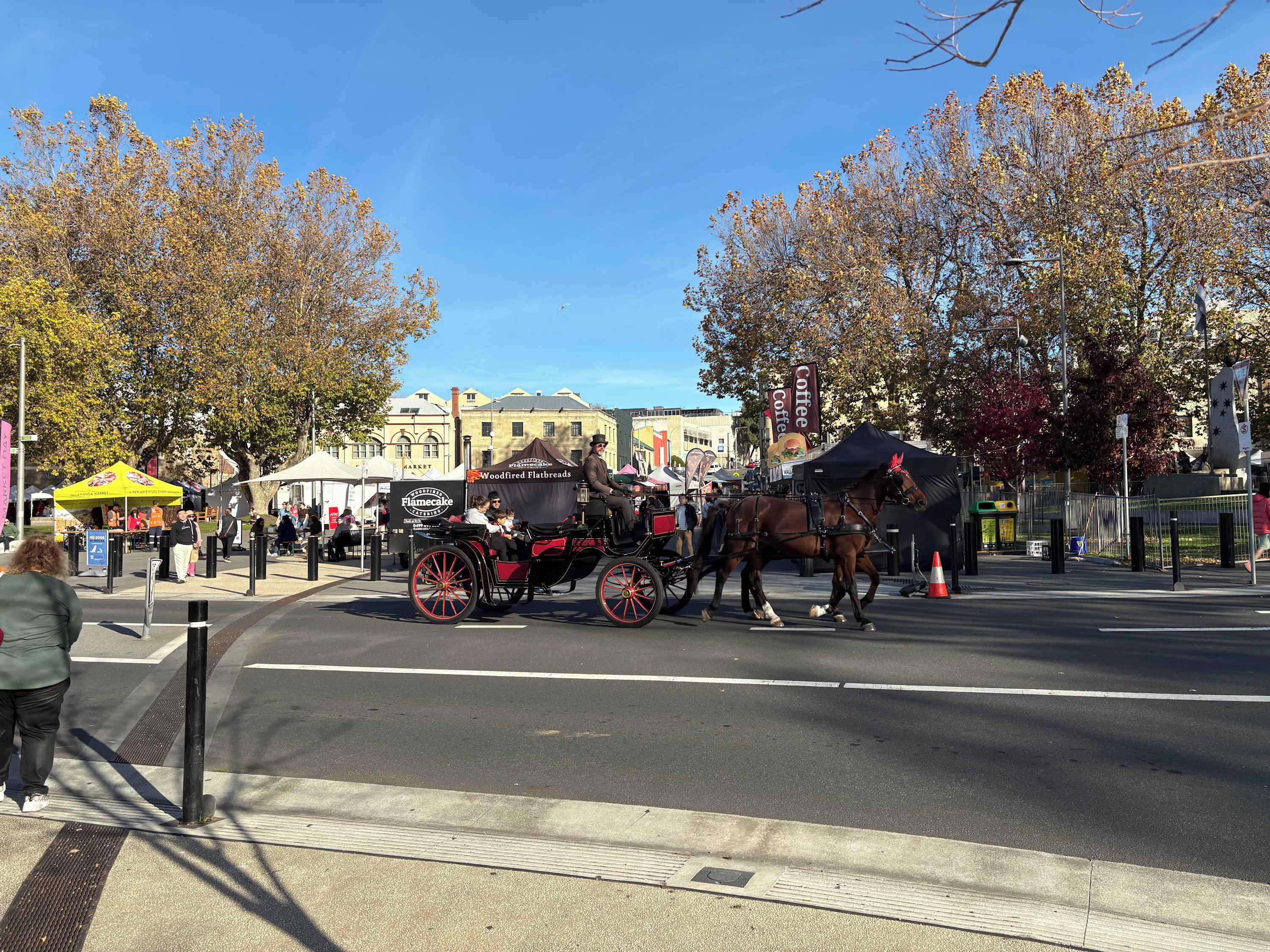 En hästdragen vagn på en stadsgata, med byggnader och träd i bakgrunden.