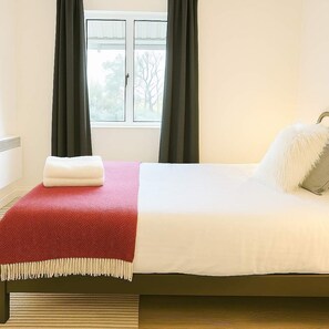 Una cama bien hecha con una colcha blanca y roja, una almohada blanca y una pequeña bolsa blanca al lado.