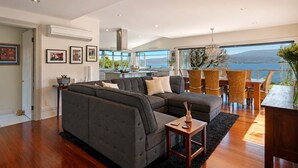 A modern living room with a sectional sofa, dining area with wicker chairs, and a view of the sea. - "Casa Con Vista" Luxury Waterfront Home-Sleeps 10. (Tranmere)