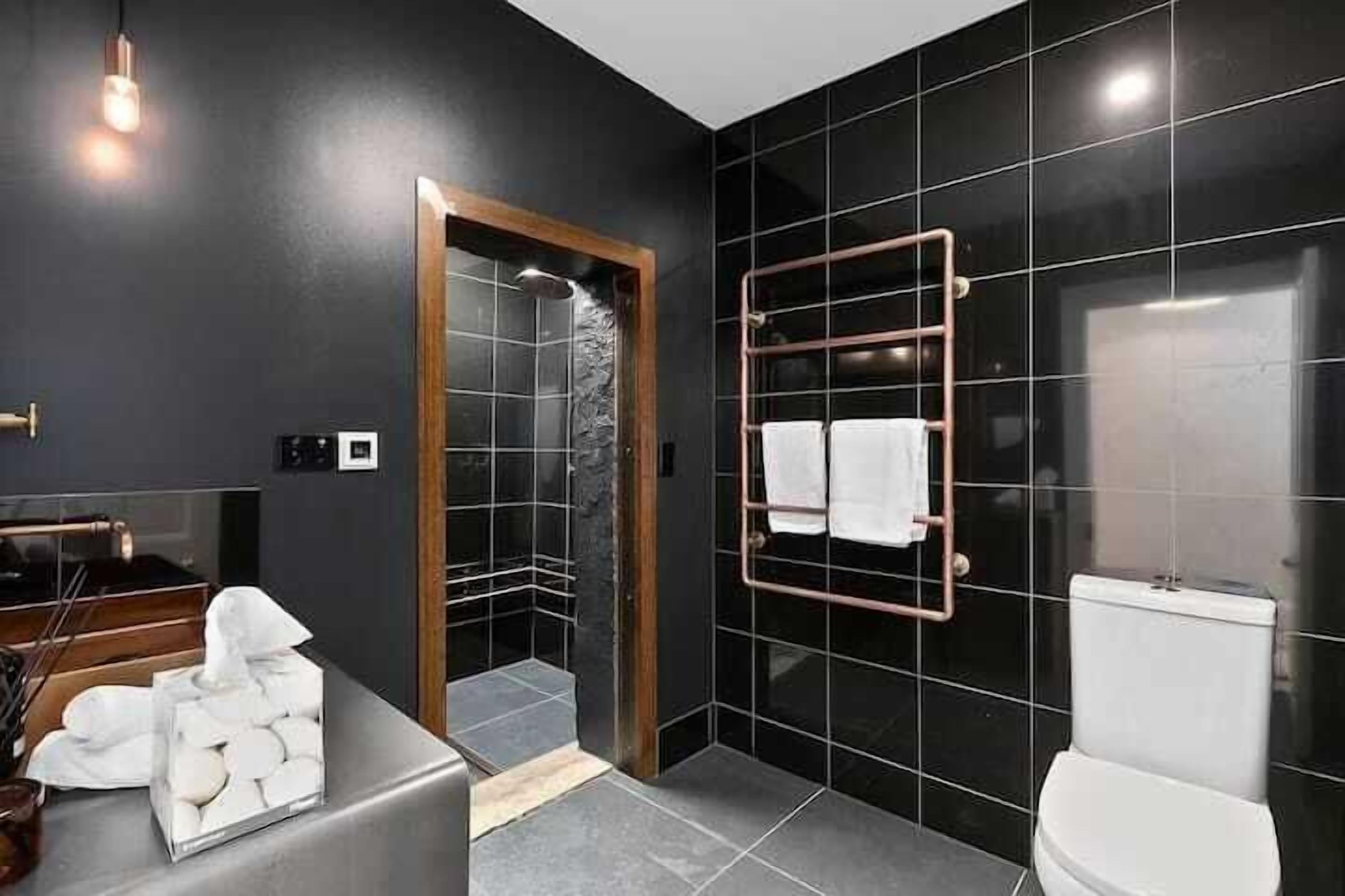 A modern bathroom with black tiles, a white toilet, a towel rack, and a shower area.