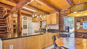 A rustic kitchen with wooden cabinets, a central island, and a dining area with a wooden table and chairs. - Classic Colorado Log Home w/ Mountain Views! (Florissant)
