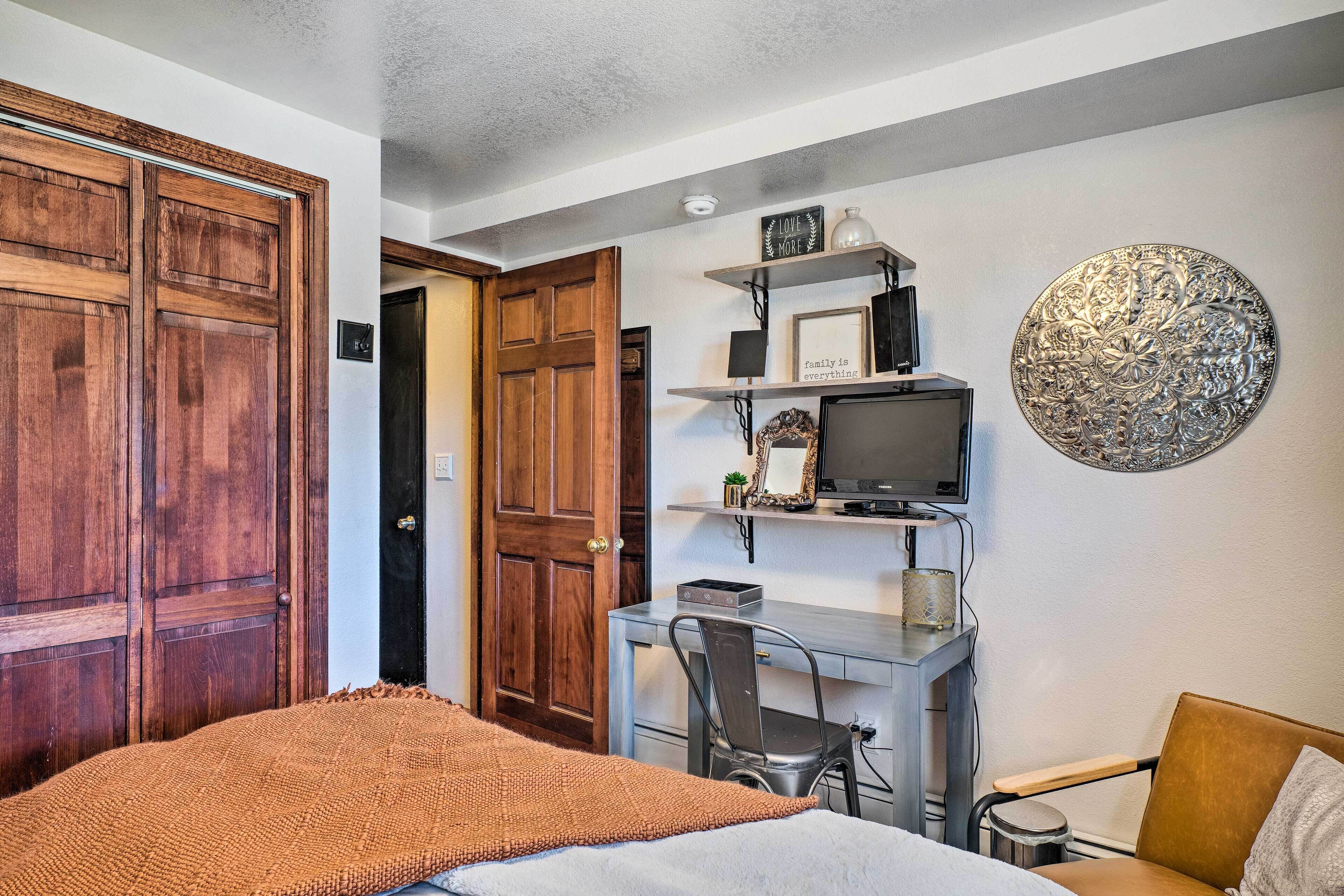 A bedroom with a bed, a desk with a chair, a television, and a decorative wall piece.
