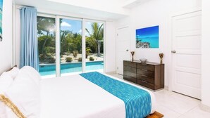 A bedroom with a large bed, a view of a swimming pool, and a dark wooden dresser. - Your tropical escape 2-bedroom villa with pool, 250 yards to Grace Bay Beach (The Bight Settlement)