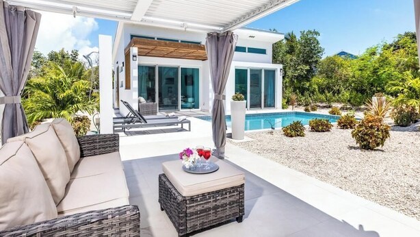 A covered outdoor area with a pool, wicker furniture, and a view of a modern house. - Your tropical escape 2-bedroom villa with pool, 250 yards to Grace Bay Beach (The Bight Settlement)