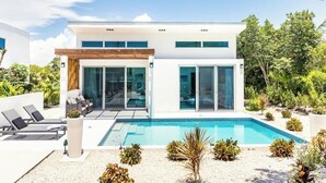 A modern two-story house with a swimming pool, large windows, and a patio area with lounge chairs. - Your tropical escape 2-bedroom villa with pool, 250 yards to Grace Bay Beach (The Bight Settlement)