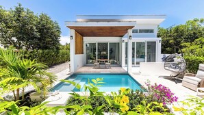 Ein modernes Haus mit Schwimmbad, einer Terrasse mit Tisch und Stühlen sowie einem Garten mit verschiedenen Pflanzen.