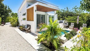 Ein modernes, zweistöckiges Haus mit Pool, Sitzgelegenheiten im Freien und üppiger Bepflanzung.