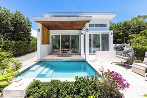 Ett modernt hus med en swimmingpool, utomhusmöbler och frodig grönska.