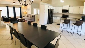 A modern kitchen with white cabinets, a black refrigerator, and a dining area with a large table and chairs. - Cul-de-sac Hideaway • Cozy Pet-Friendly Mid-Term Stay, Short Drive to Beach (St. Augustine)
