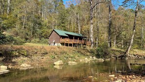 Une cabane dotée d’une terrasse donnant sur une rivière, entourée d’arbres.