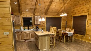 L’intérieur d’un chalet rustique, avec une cuisine en bois, un coin repas et de grandes fenêtres.