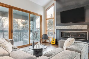 Ein modernes Wohnzimmer mit Kamin, einem großen Fernseher und Blick auf eine verschneite Landschaft durch große Fenster.