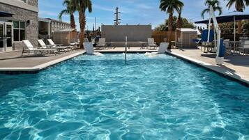 A swimming pool with clear water, surrounded by lounge chairs and palm trees.