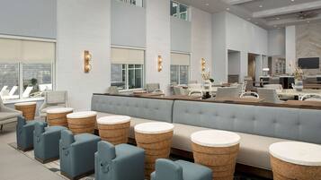 A modern hotel lobby with a large seating area, a reception desk, and large windows.
