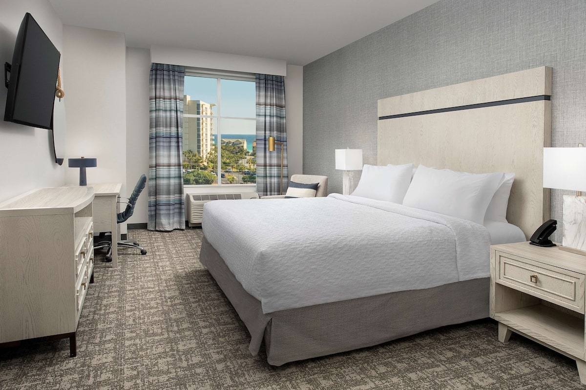 Ein Hotelzimmer mit einem großen Bett, einem Schreibtisch, einem Stuhl, einem Fernseher und Blick auf die Stadt.