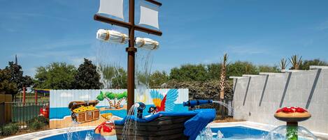 A swimming pool with a pirate ship fountain, surrounded by a fence and trees.
