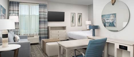 Une chambre d’hôtel moderne équipée d’un téléviseur à écran plat, d’un lit, d’un bureau, d’une chaise, d’une petite table et d’un canapé.