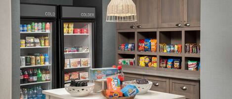 Una kitchenette equipada con refrigerador, congelador y alacenas llenas de botanas y bebidas.