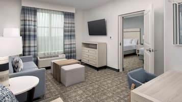Habitación de hotel con sofá, una mesita, televisor montado en la pared, cómoda y cama con cabecera.