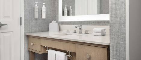 A modern bathroom with a large mirror, a sink, a towel rack, and toiletries on the wall.