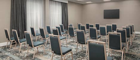 Ein Konferenzraum mit Reihen von Stühlen, einer großen Leinwand und einem gemusterten Teppich.