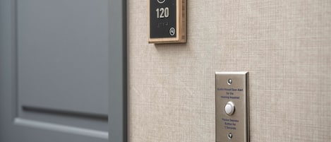 A door with a number plate reading "202 120" and a button labeled "Audio-Visual Door Alert for the Hearing Impaired" with instructions to "Please Depress Button for 5 Seconds".