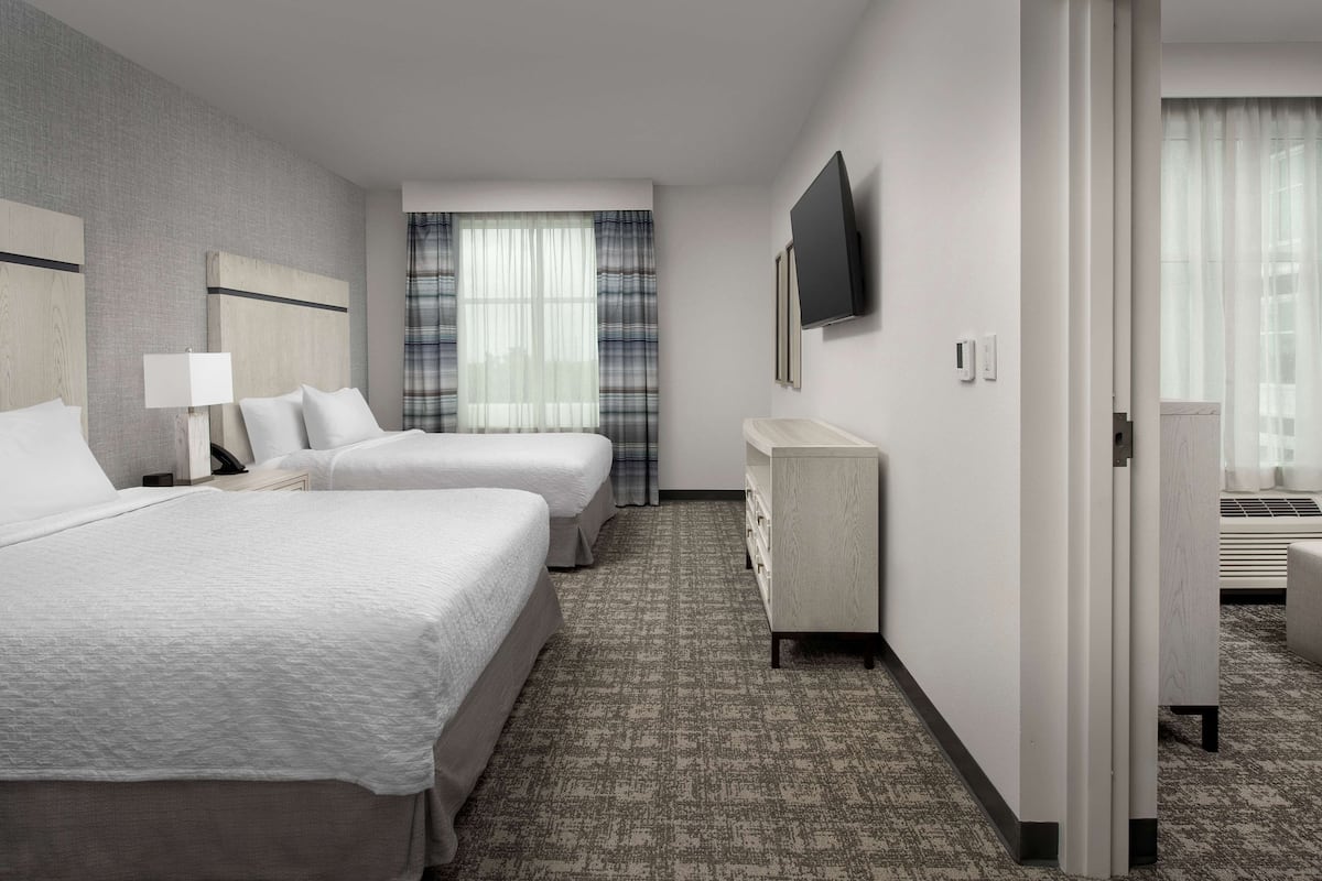 Ein Hotelzimmer mit zwei Betten, einem Fernseher, einem Schreibtisch und einem Fenster mit Vorhängen.