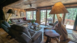 Ein gemütliches Blockhäuschen-Interieur mit Holzbalkendecke, einer Couch, einem Couchtisch und einer besonderen Lampe.
