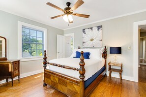 Relax in a classic four-poster bed with a modern twist, featuring a ceiling fan and a large window with an outdoor view.