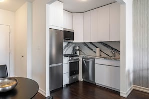 Una cocina moderna con armarios blancos, electrodomésticos de acero inoxidable, salpicadero de mármol y una mesa de comedor redonda.