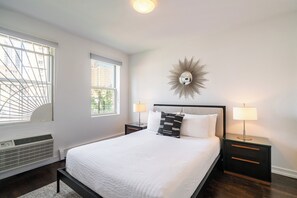 Un dormitorio con cama, dos mesitas de noche, un espejo en la pared y una ventana con persianas.