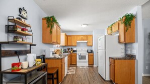 Eine kompakte Küche mit Holzausbau, einer Mikrowelle, einem Herd und einem Kühlschrank. Regale mit Küchenutensilien und eine Uhr an der Wand.