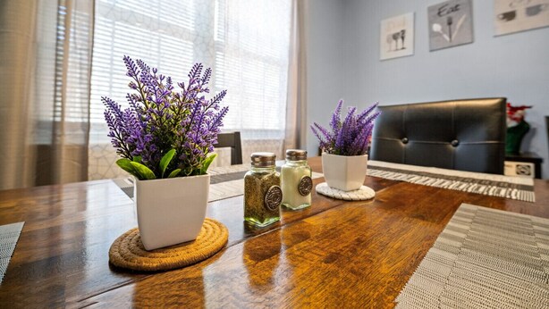 Ein modernes Wohnzimmer mit einem Holztisch, zwei Lavendelpflanzen in Töpfen und einem schwarzen Ledersofa.