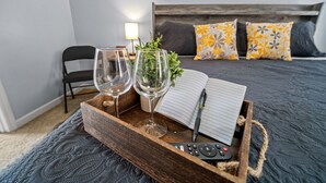 Habitación de hotel con una cama, una mesita de noche con una bandeja que sostiene dos vasos, un control remoto y una libreta.