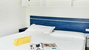 Una habitación de hotel con una cama grande, ropa de cama blanca, un cabecero azul y una revista sobre la cama.
