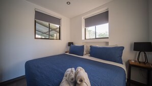 Una camera da letto con un letto grande, due finestre, un comodino con una lampada e un paio di asciugamani sul letto.