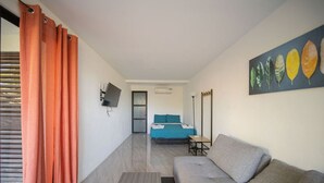 Una camera moderna con un divano grigio, un letto con lenzuola blu, un quadro con foglie e un televisore a parete.