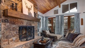 Una chimenea de piedra con una decoración de cabeza de ciervo, techo de madera, un sofá y cortinas estampadas.