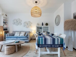A modern living room with a sofa, a dining table with a striped tablecloth, a hanging light fixture, and decorative wall art.