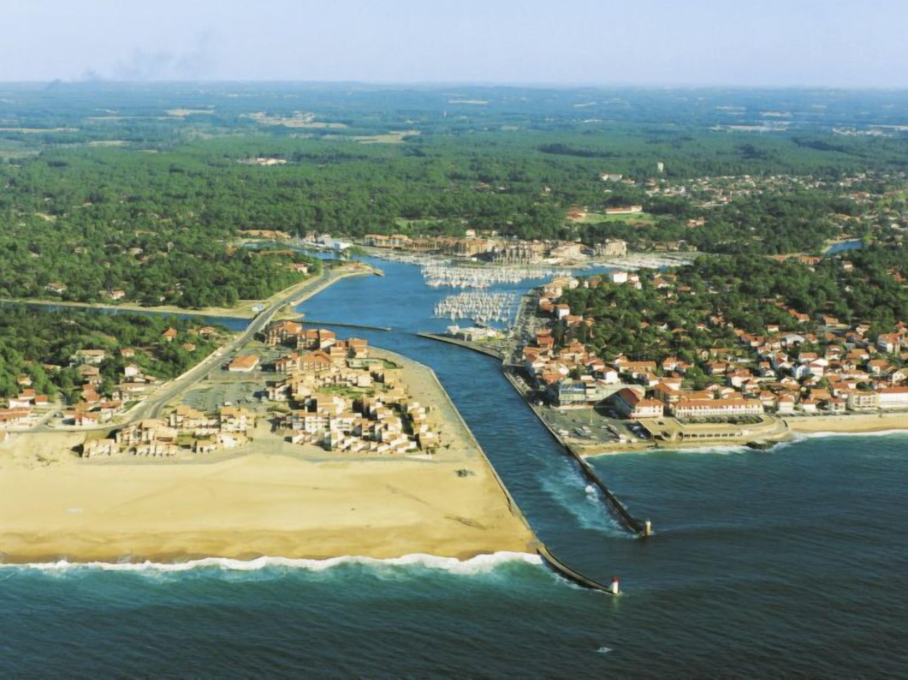 An aerial view of a coastal town with a beach, marina, and dense residential area.